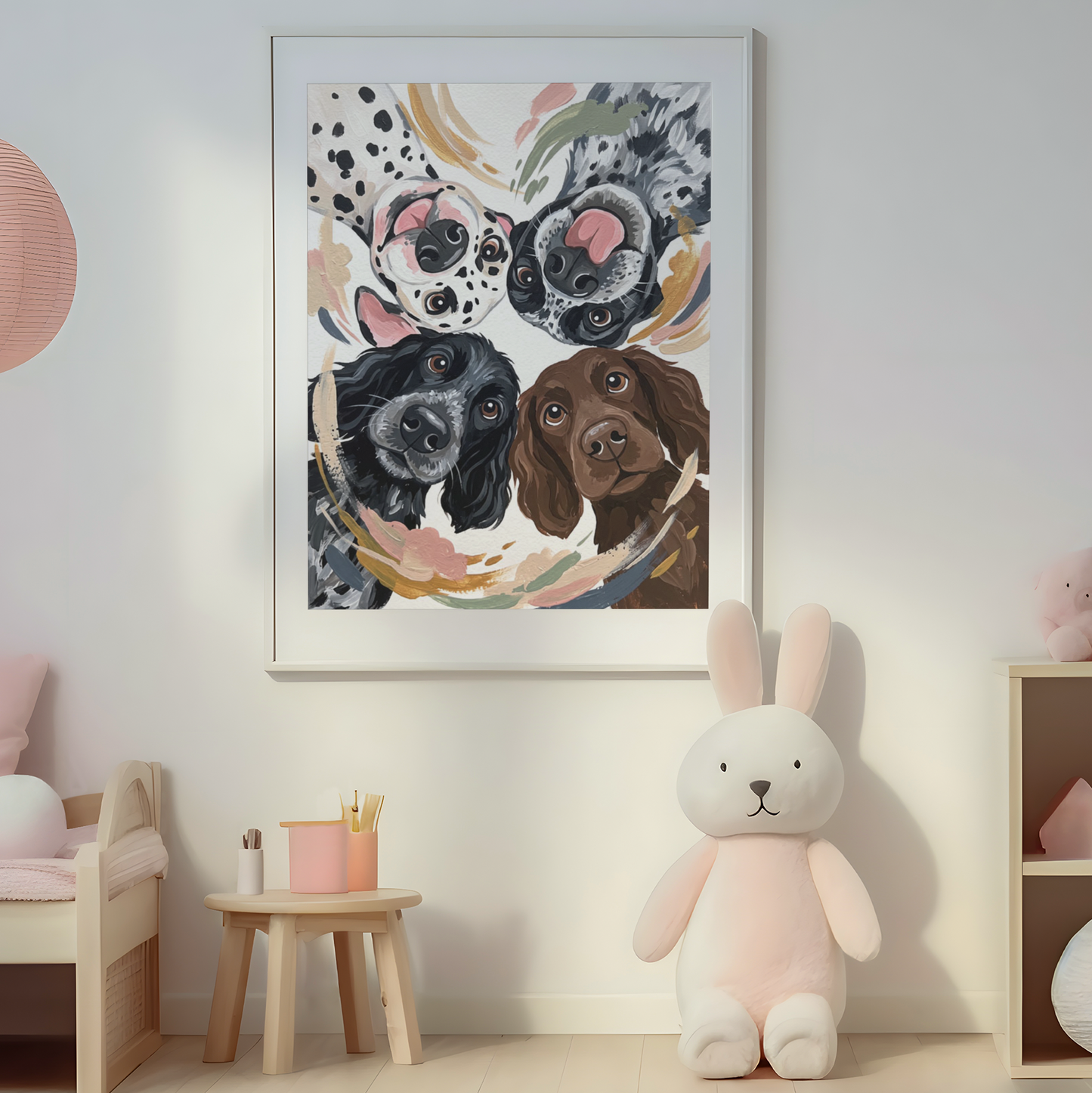 A framed vertical art print featuring a colorful watercolor-style illustration of four dogs, displayed on a light gray wall in a styled children's room with a pink bench, hanging lamp, bunny plush, and wooden shelf.