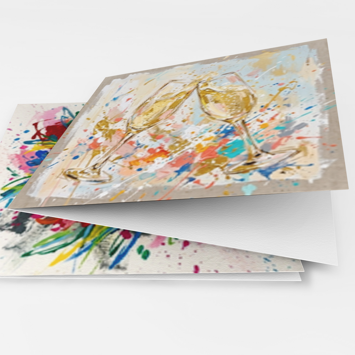 Two overlapping greeting cards with an abstract wine-themed design, featuring two wine glasses, colorful paint splatters, and a gold foil effect, displayed on a clean white background.